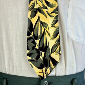 May include: A yellow and green patterned tie with a leaf design. The tie is made of silk and has a classic shape.