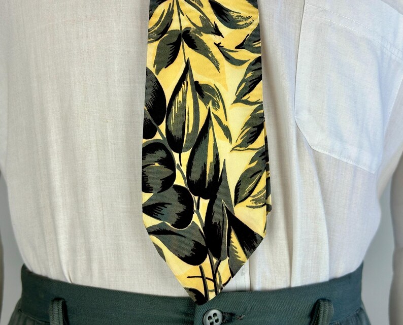 May include: A yellow and green patterned tie with a leaf design. The tie is made of silk and has a classic shape.