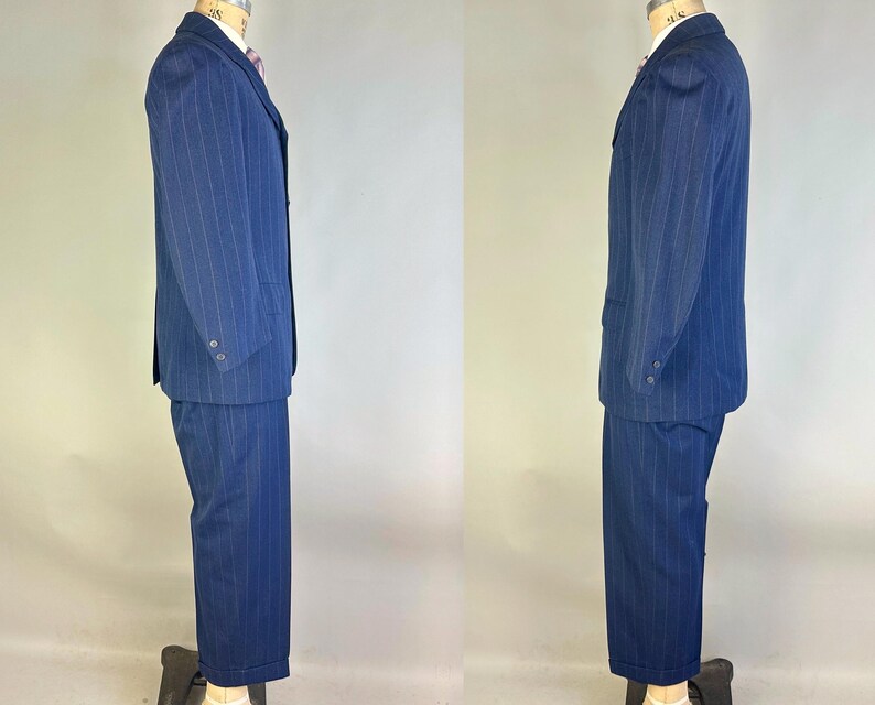 Puede incluir: Un traje azul marino con un sutil patr&oacute;n de rayas verticales. El conjunto consta de una americana de botonadura sencilla con solapas de muesca y dos botones en los pu&ntilde;os, combinada con pantalones a juego de corte recto.