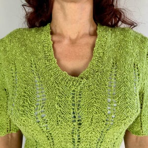 May include: A lime green, short-sleeved knit top with a V-neck. The top features a textured, open-weave design. The sleeves are short and the neckline is finished with a ribbed edge. The knitwear is a bright, solid color.
