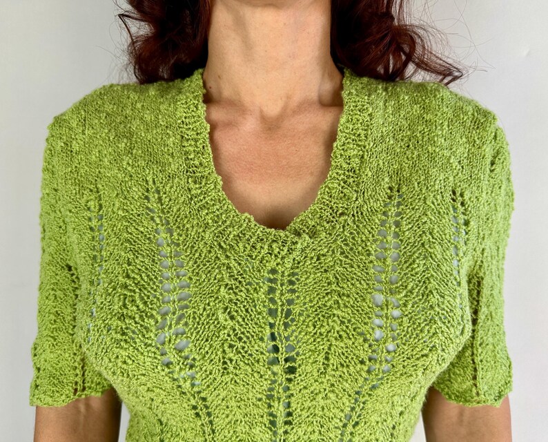 May include: A lime green, short-sleeved knit top with a V-neck. The top features a textured, open-weave design. The sleeves are short and the neckline is finished with a ribbed edge. The knitwear is a bright, solid color.