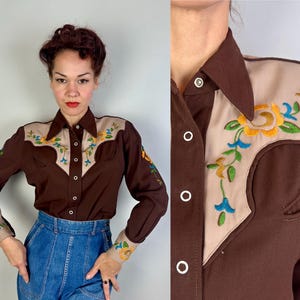May include: A long-sleeve button-down shirt in dark brown with beige yokes on the shoulders and cuffs. The beige sections feature colourful floral embroidery in yellow, green, and blue. The shirt has a pointed collar and white snap buttons.