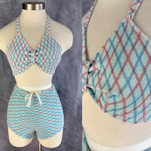 May include: A vintage two-piece swimsuit set. The halter-top bikini and high-waisted shorts are light blue with a red and blue plaid pattern. The top has a bow detail at the centre. The shorts have a drawstring waist.