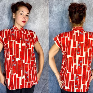 Pode incluir: Uma camisa de manga curta com bot&otilde;es, apresentando um fundo creme com um padr&atilde;o repetitivo de pain&eacute;is retangulares vermelhos verticais. Os pain&eacute;is vermelhos cont&ecirc;m caligrafia preta de estilo asi&aacute;tico e pequenos detalhes florais azuis.
