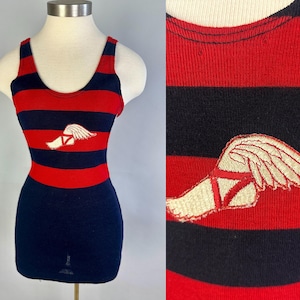 May include: A sleeveless tank top featuring horizontal red and navy blue stripes. The chest area displays an embroidered patch of a white winged foot with red detailing. The garment has a scoop neckline and a fitted silhouette on a mannequin.