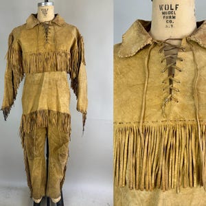 Könnte beinhalten: Ein braunes Lederoutfit mit Fransenbesatz. Das Outfit besteht aus einem langärmeligen Hemd, einem Rock und einer Hose. Das Hemd hat einen Schnürverschluss vorne und der Rock und die Hose haben Fransenbesatz.