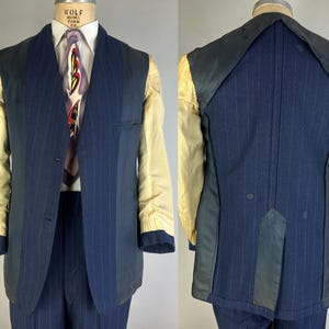 Puede incluir: Un blazer azul marino de rayas diplom&aacute;ticas con cuello chal, que presenta un interior parcialmente forrado con forro de mangas color crema, cierre frontal de dos botones y una abertura trasera, sobre un maniqu&iacute; con camisa y corbata.