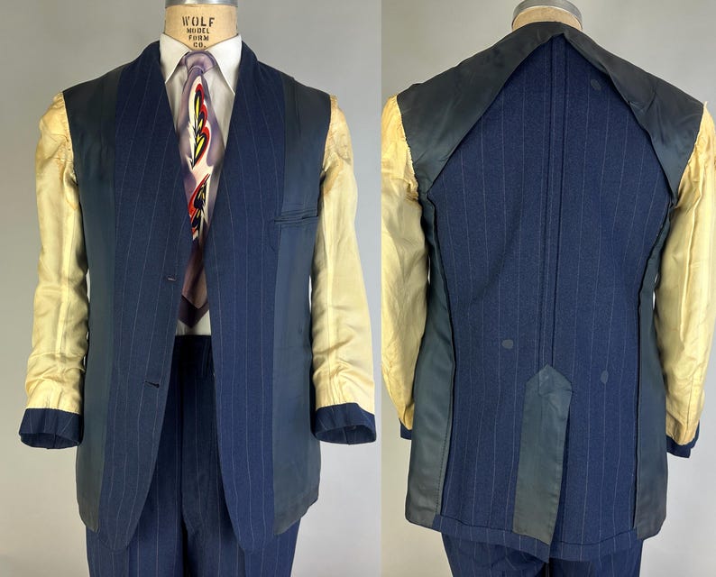 Puede incluir: Un blazer azul marino de rayas diplom&aacute;ticas con cuello chal, que presenta un interior parcialmente forrado con forro de mangas color crema, cierre frontal de dos botones y una abertura trasera, sobre un maniqu&iacute; con camisa y corbata.