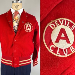 Op de afbeelding: Rood wollen varsity jack met een witte en rode gestreepte gebreide kraag, manchetten en tailleband. Het jack heeft een knoopsluiting en een groot geborduurd embleem op de linkerborst met de tekst "Devils A Club".
