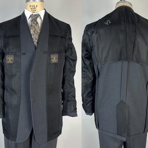 May include: A charcoal gray blazer shown from the front and back, featuring a partial black lining, a shawl collar, and a patterned necktie. The interior lining displays two rectangular labels with text and the number 42 written on the back fabric.