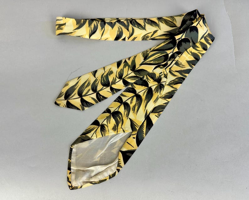 May include: A yellow and black patterned tie with a leaf design. The tie is made of silk and has a pointed tip.
