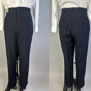 May include: High-waisted dark navy trousers featuring a button closure, belt loops, and cuffed hems. The pants are shown from both the front and back views, paired with a white long-sleeved button-down shirt. The fabric has a subtle texture.