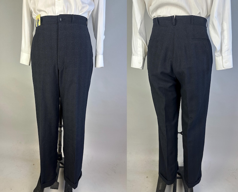 May include: High-waisted dark navy trousers featuring a button closure, belt loops, and cuffed hems. The pants are shown from both the front and back views, paired with a white long-sleeved button-down shirt. The fabric has a subtle texture.