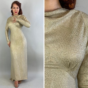 May include: A long, gold-colored dress with long sleeves and a high neckline. The dress has a textured surface and a fitted silhouette. The dress is floor-length and appears to be made of a shimmering fabric.