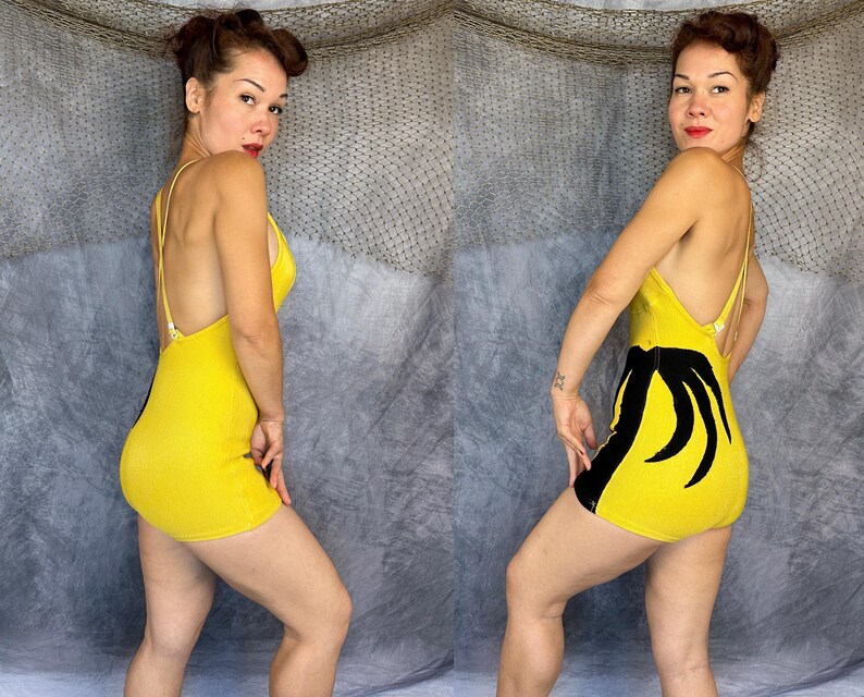 May include: A yellow one-piece bodysuit featuring thin shoulder straps and a black graphic design on the side. The garment has a low-cut back with crisscross straps and a fitted silhouette that extends to the upper thigh, showcasing a vibrant color.