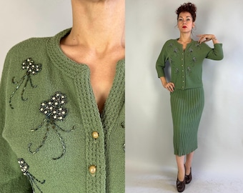 May include: A green cardigan and skirt set with beaded floral embellishments. The cardigan has a V-neck and button closure. The skirt is a-line and knee-length.