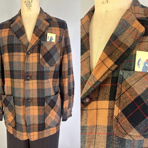 Könnte beinhalten: Ein langärmeliger Blazer mit einem braunen, schwarzen und grauen Karomuster, einem steigenden Revers, drei Knöpfen auf der Vorderseite und drei aufgesetzten Taschen. Eine kleine rechteckige Karte mit einem blauen Pfau ist eingesteckt.