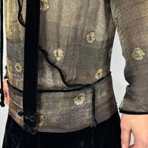 May include: A sheer, gold-toned blouse with a black velvet trim and tie. The blouse has a floral pattern and a fitted silhouette.