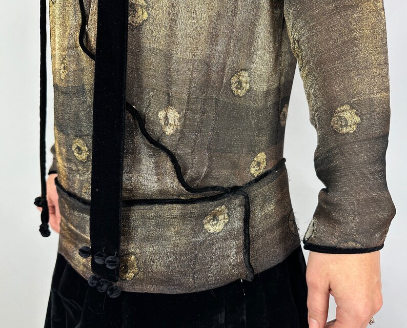 May include: A sheer, gold-toned blouse with a black velvet trim and tie. The blouse has a floral pattern and a fitted silhouette.