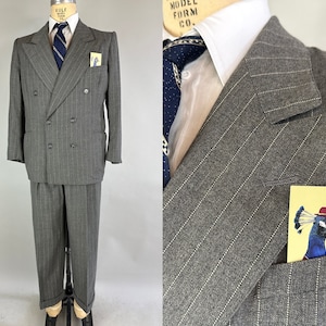 Puede incluir: Un traje cruzado de rayas grises con camisa blanca de cuello, corbata azul oscuro estampada y un pañuelo de bolsillo con la ilustración de un pavo real con un pequeño sombrero rojo, presentado sobre un maniquí.