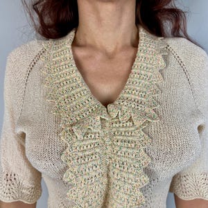 May include: A cream-colored crocheted sweater with a scalloped, multi-colored trim around the neckline.