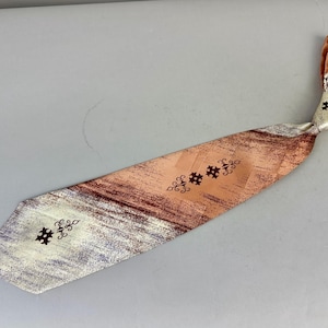 Puede incluir: Una corbata vintage con un patrón único. La corbata presenta una paleta de colores melocotón, marrón y plateado, con una apariencia texturizada. Tiene formas geométricas decorativas de color marrón oscuro. La corbata está anudada en la parte superior, mostrando su diseño.