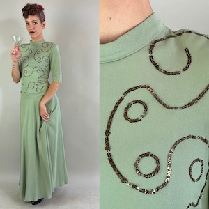 May include: A sage green maxi dress with a fitted bodice and a flowing skirt. The bodice features a unique design of brown sequins in a swirling pattern.