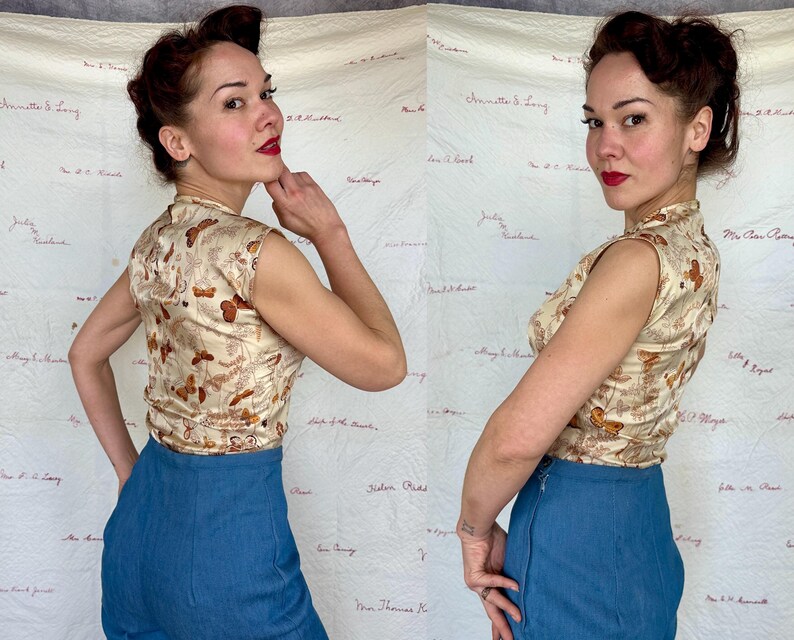 May include: A sleeveless, cream-colored top with a butterfly pattern and a mandarin collar. The top is paired with high-waisted, blue denim pants. The outfit is vintage-inspired, with a retro aesthetic. The background is a white fabric with handwritten text.