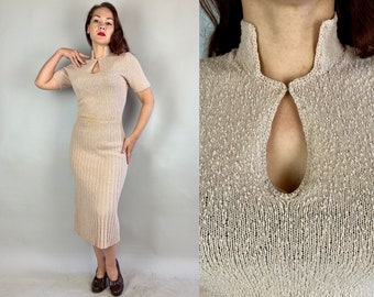 Puede incluir: Un vestido de punto beige con cuello alto y una abertura de ojo de cerradura en el escote. El vestido tiene un corpiño ajustado y una falda recta.