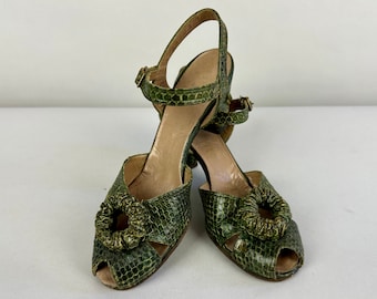 Op de afbeelding: Een paar groene slangenleren sandalen met een decoratieve gesp en een rond ontwerp op de teen.
