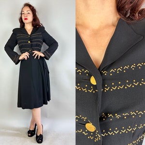 May include: A black vintage dress with a matching jacket. The jacket features gold-colored embellishments and buttons. The dress has a midi-length skirt and a fitted waist. The outfit is a classic style.