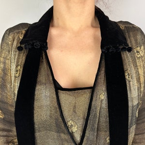 May include: A gold sheer blouse with a black velvet collar and trim. The collar has a row of black pom-poms along the edge.