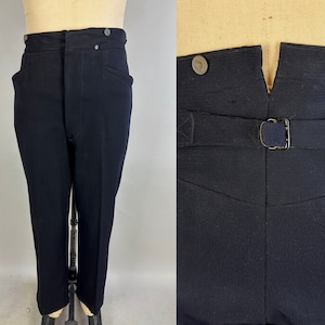 Könnte beinhalten: Eine dunkelblaue Hose mit hoher Taille und Knopfleiste. Die Hose hat Gürtelschlaufen und eine Schnalle auf der Rückseite.