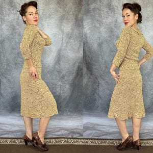 May include: A vintage two-piece knit dress in a speckled pattern of tan and burgundy. The set includes a long-sleeved top and a knee-length skirt. The model is wearing matching patterned heels.