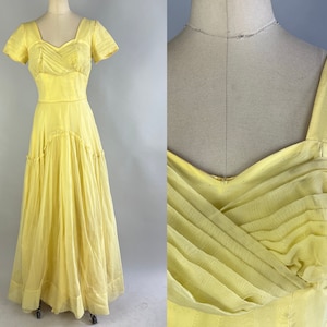 Könnte beinhalten: Ein vintage hellgelbes Kleid mit einem Sweetheart-Ausschnitt und kurzen Ärmeln. Das Oberteil hat einen plissierten Stoff, und der Rock fällt bis zum Boden. Das Kleid wird auf einer Schaufensterpuppe präsentiert.