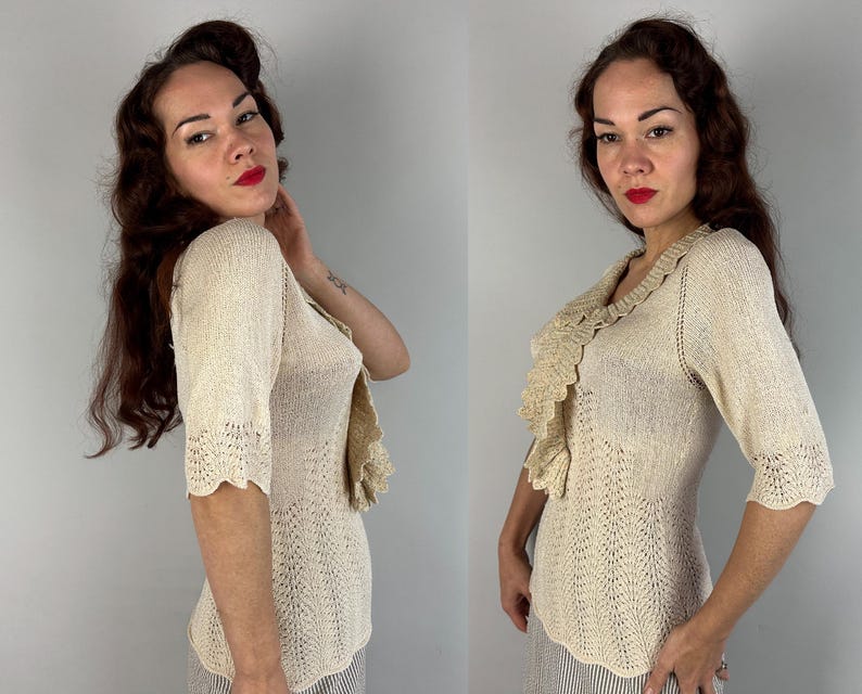 May include: A cream-colored knitted sweater with a ruffled neckline and short sleeves. The sweater is made of a delicate, open-weave fabric.