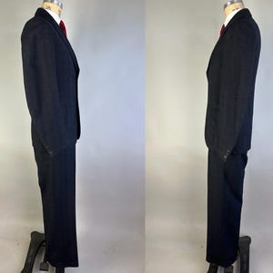 May include: A dark charcoal gray suit consisting of a single-breasted blazer with notched lapels and matching trousers. The blazer features a white collared shirt underneath with a solid red necktie. The suit is displayed on a mannequin.