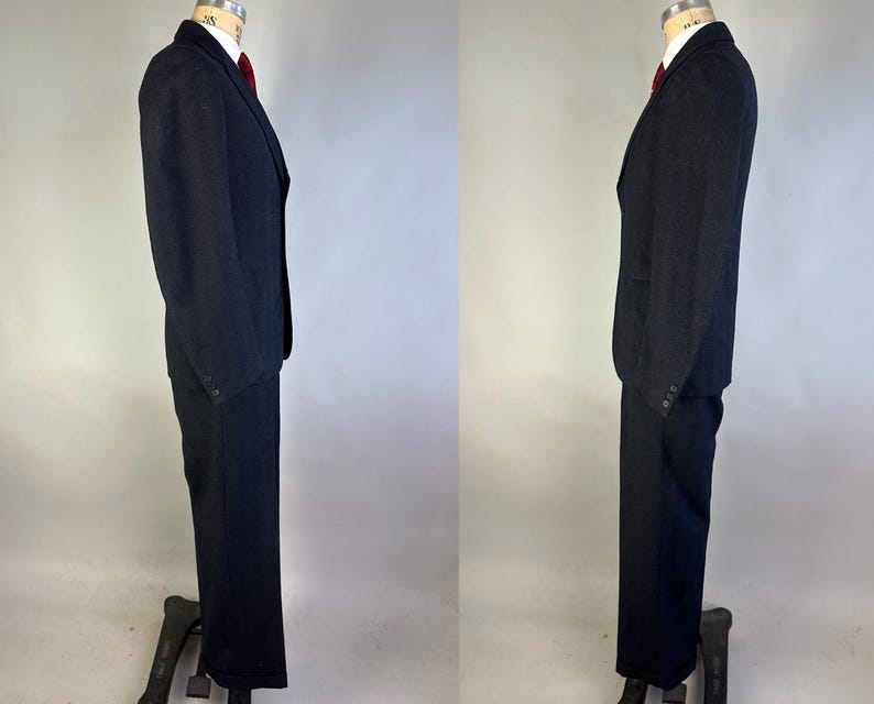 May include: A dark charcoal gray suit consisting of a single-breasted blazer with notched lapels and matching trousers. The blazer features a white collared shirt underneath with a solid red necktie. The suit is displayed on a mannequin.