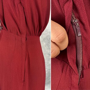 May include: A close-up of a burgundy dress with a zipper detail. The dress has a fitted bodice and a slightly flared skirt. The zipper is visible on the side of the dress. The dress has a textured fabric and a subtle sheen.