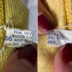 May include: A yellow knit garment featuring a white fabric tag with blue text that reads FINE QUALITY RAYON COTTON AND ELASTIC NOT RETURNABLE. The tag also displays the size S6 in blue ink, with visible stitching along the edge of the yellow fabric.