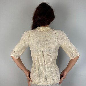 May include: A white crocheted sweater with a delicate lace pattern and short sleeves.