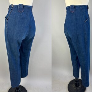 May include: High-waisted dark blue denim pants featuring a side zipper closure, a structured waistband with belt loops, and a tapered leg silhouette. The garment is shown from two angles, highlighting the side seam zipper and the back pocket placement.