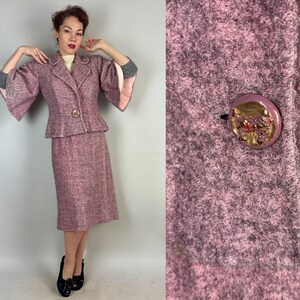 Może przedstawiać: Garniturowy komplet w kolorze różowym z tweedu, składający się z żakietu i spódnicy. Żakiet ma szeroki kołnierz, długie rękawy i zapięcie na guziki. Spódnica sięga do kolan i ma prosty krój.