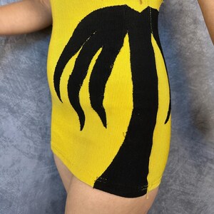 May include: A bright yellow ribbed knit garment featuring a bold, black graphic design of a palm tree silhouette that extends vertically along the side. The fabric has a distinct textured, vertical ribbed pattern throughout the yellow sections.