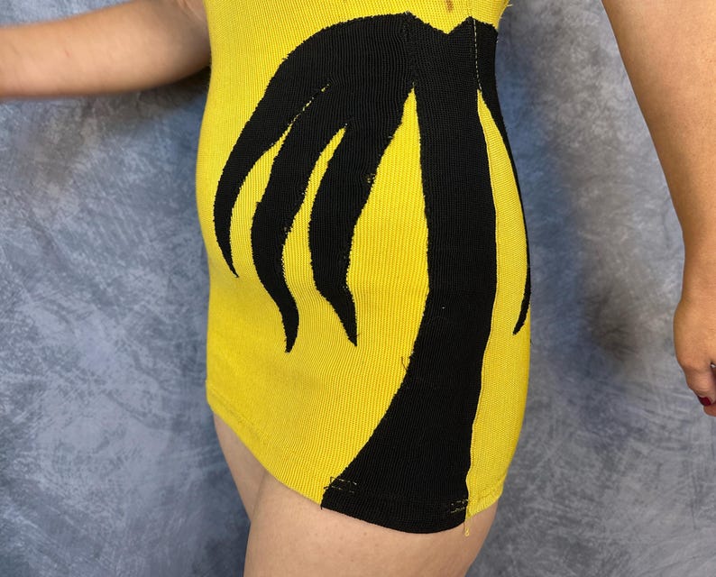 May include: A bright yellow ribbed knit garment featuring a bold, black graphic design of a palm tree silhouette that extends vertically along the side. The fabric has a distinct textured, vertical ribbed pattern throughout the yellow sections.