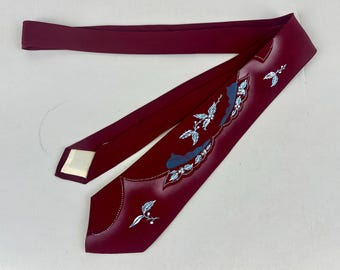 May include: A deep burgundy necktie featuring a decorative scalloped edge design in white and light blue. The tie is adorned with hand-painted white and light blue leaf and berry motifs, accented by delicate white dotted lines along the edges.