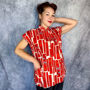 Pode incluir: Uma camisa de manga curta com um padr&atilde;o vibrante de blocos retangulares vermelhos e brancos com pequenos detalhes florais azuis. A camisa apresenta uma gola mandarim, uma carcela de bot&otilde;es frontal e dois bolsos na parte inferior.