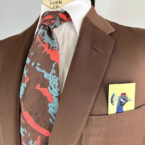 May include: A brown suit jacket with a white collared shirt and a patterned tie. The tie features a design with brown, red, and blue elements. A small card with a peacock illustration in a pocket adds a pop of color.