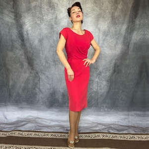 May include: A vibrant red knee-length dress featuring short cap sleeves, a rounded neckline, and a fitted bodice with subtle draping at the waist. The skirt follows a straight silhouette, ending just below the knee, creating a clean and structured look.