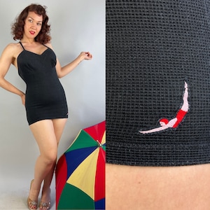 May include: A black one-piece swimsuit with a plunging neckline and a swimmer graphic on the bottom. The swimsuit is made of a textured fabric.